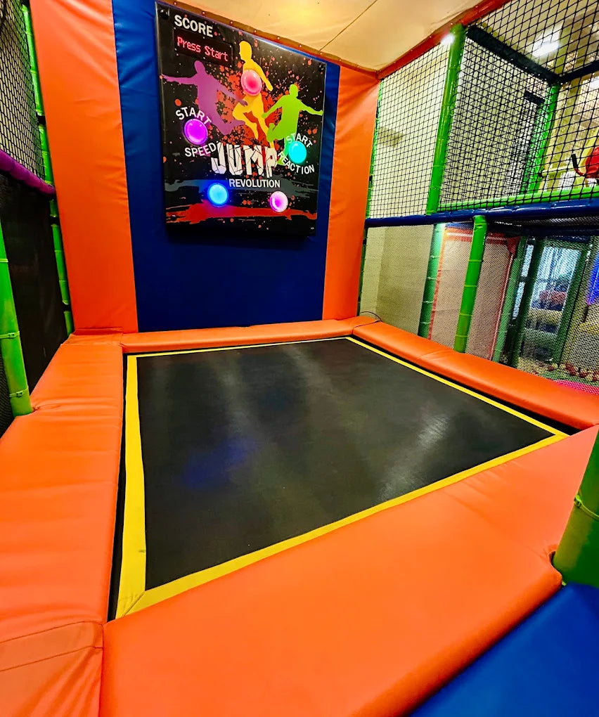 A trampoline park with a "Jump Revolution" game board and padded orange edges.