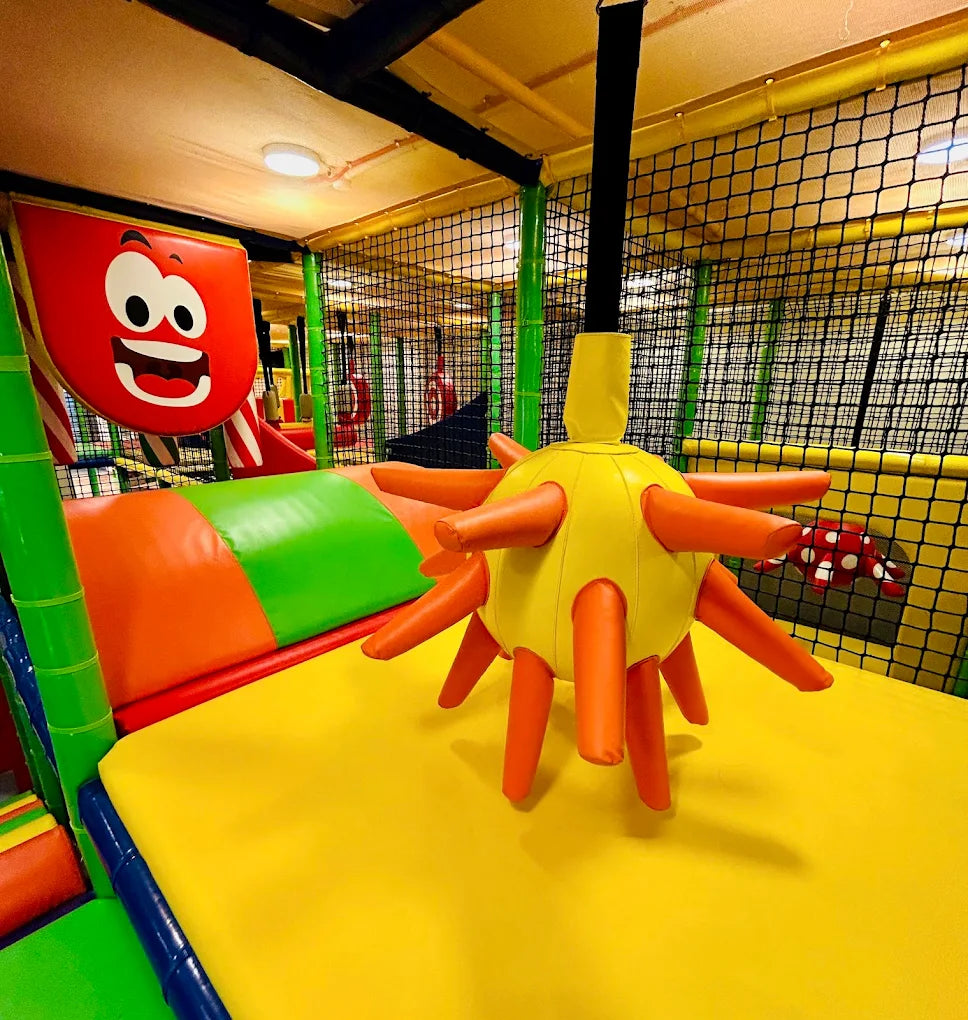 A colorful indoor playground with soft play structures and netting.