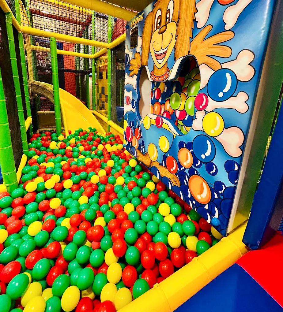 A ball pit filled with colorful balls in a children's play area, with a cartoon dog game in the background.