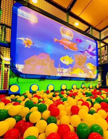 A ball pit filled with colorful balls in front of a large screen displaying an underwater scene with animated fish.