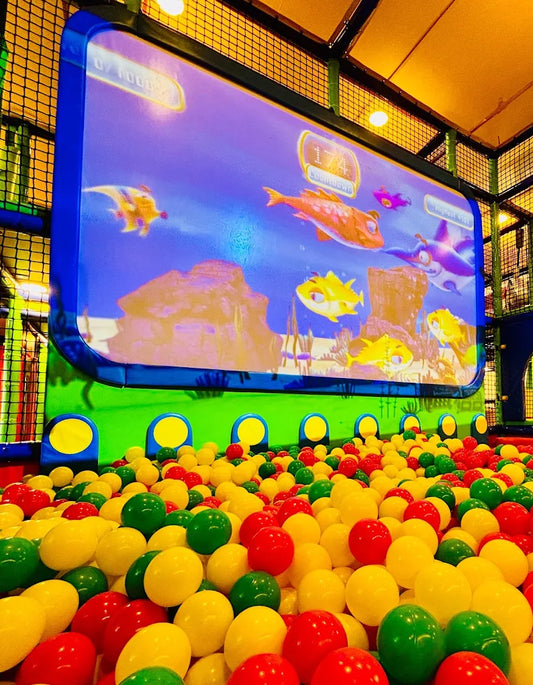 A ball pit filled with colorful balls in front of a large screen displaying an underwater scene with animated fish.