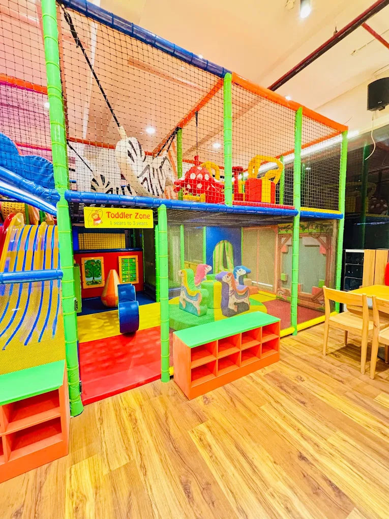 A colorful indoor playground with a toddler zone, featuring slides, soft play structures, and seating for young children.