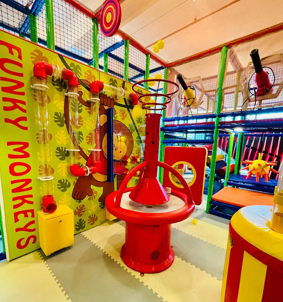 A colorful indoor playground with a red interactive game in the foreground and monkey-themed decorations.