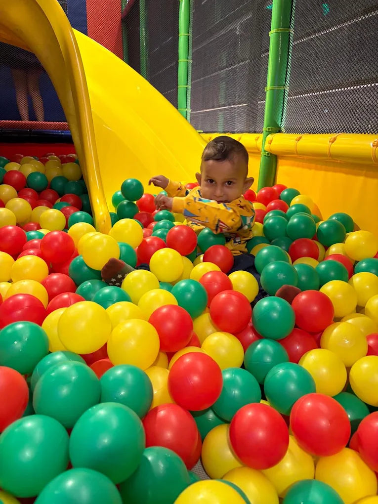 A young child plays in a ball pit with a yellow slide.