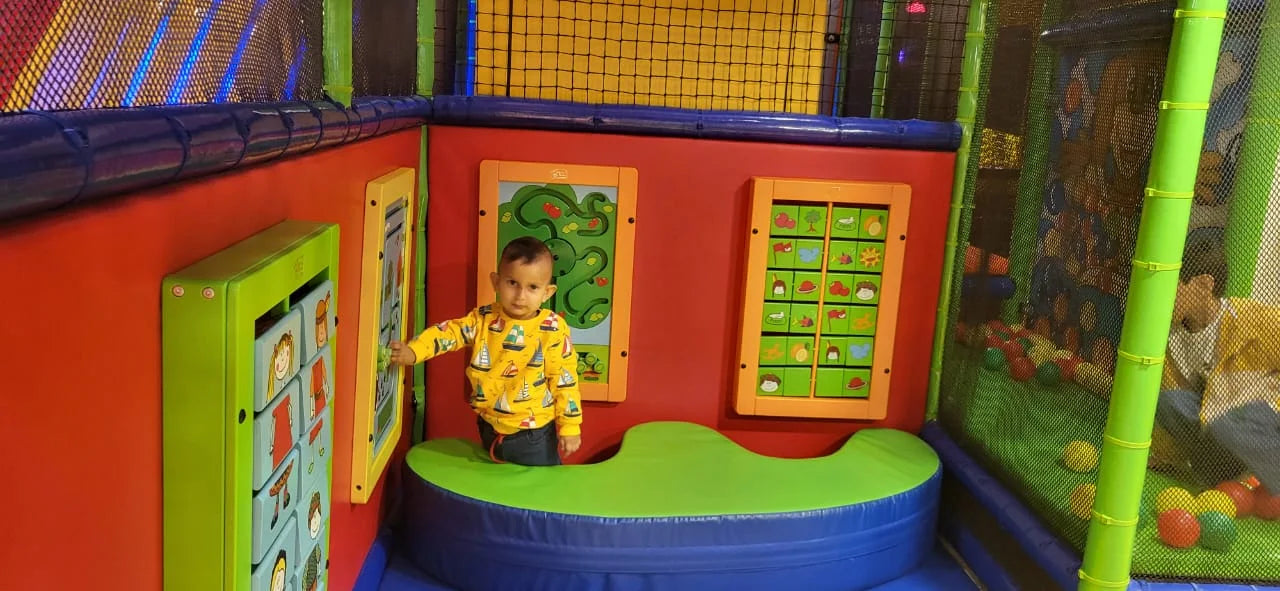 A young child plays in a colorful indoor playground with interactive wall panels.
