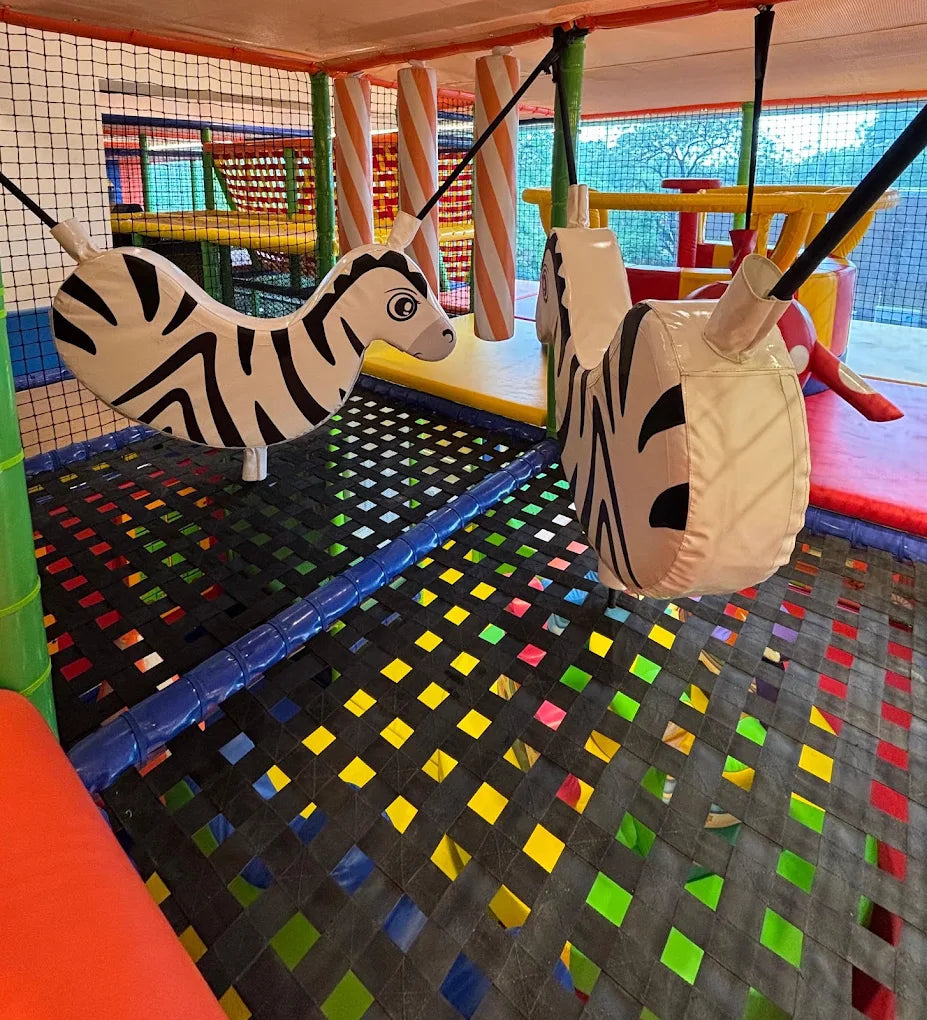 A soft play area with zebra swings over a colorful net floor.