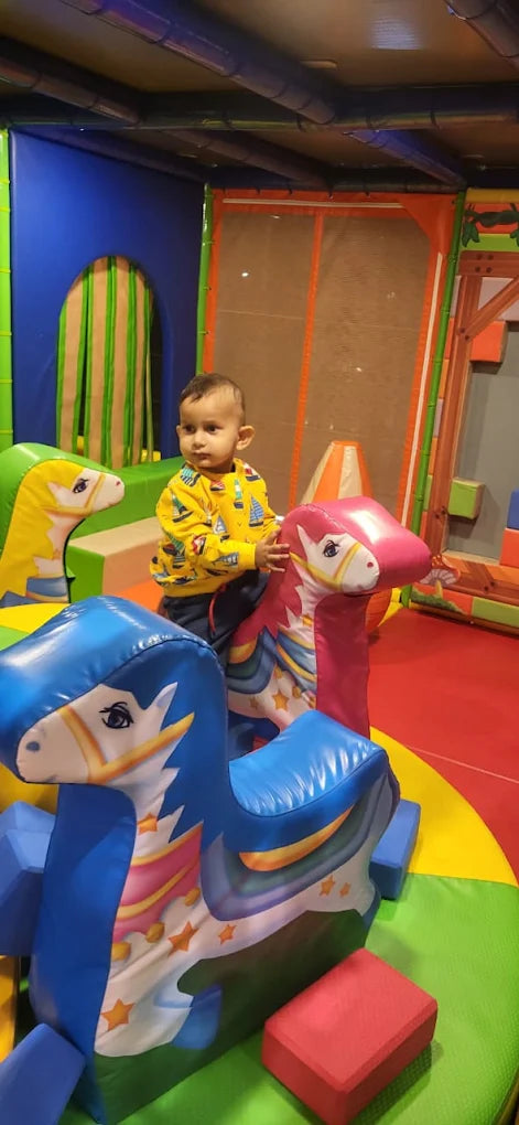 A toddler sits on a pink inflatable unicorn in a colorful indoor play area.