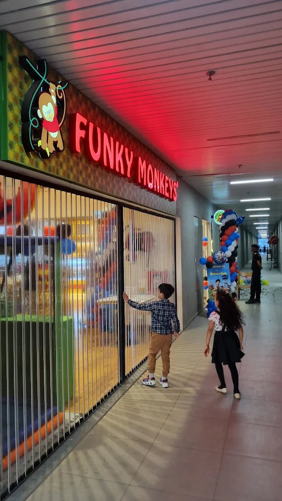 Children look into a brightly lit indoor play area called "Funky Monkeys," decorated with balloons.