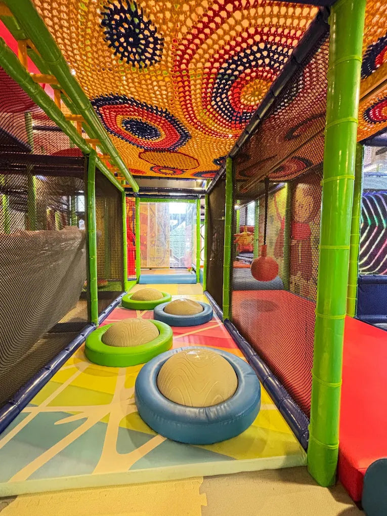 A colorful indoor playground with soft stepping stones and a netted ceiling.