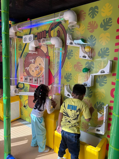 Children play with a colorful ball-tracking wall in a playful indoor playground.