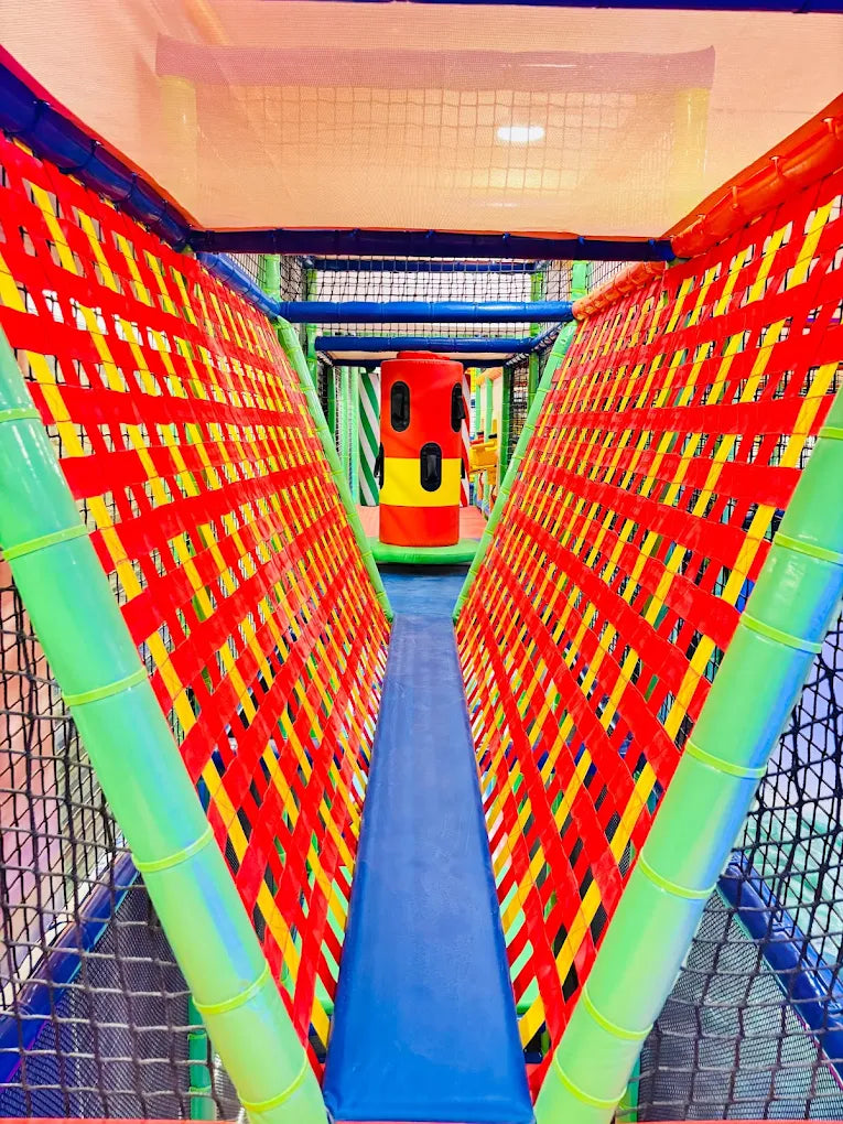 A colorful indoor playground with a netted walkway and a red and yellow tube slide.