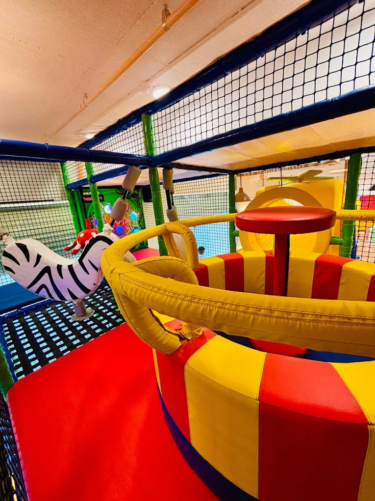 A colorful indoor playground with soft play structures and a zebra toy.