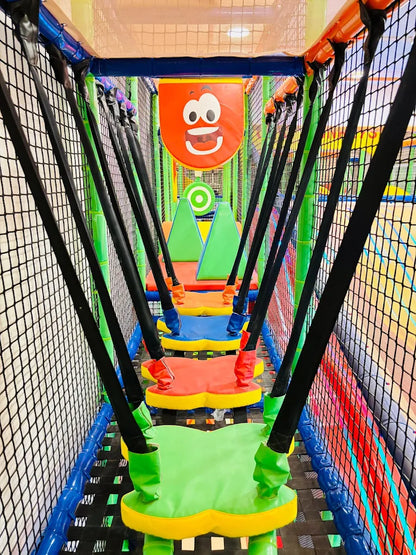 A colorful indoor playground with a rope bridge and swings for children.