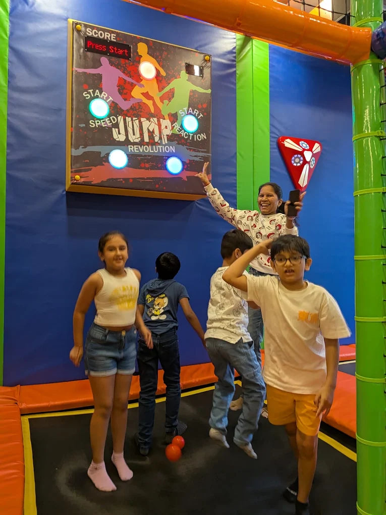 Children jump on trampolines in front of a score board at an indoor play center.