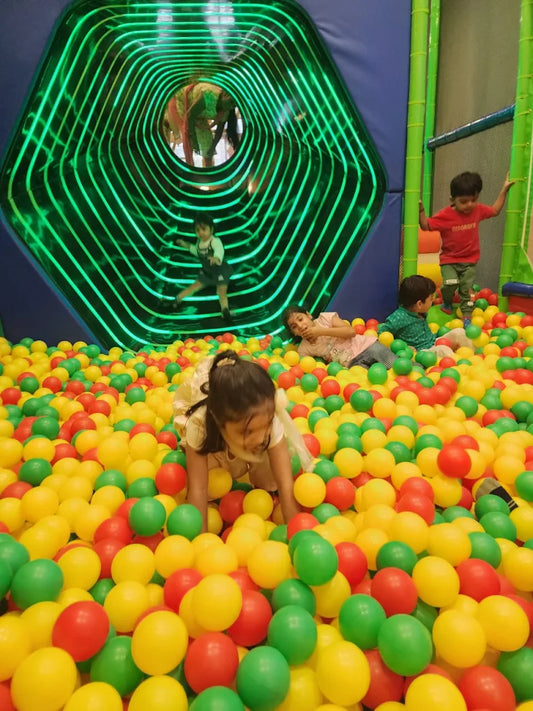 Children play in a ball pit with a green, glowing tunnel in the background.