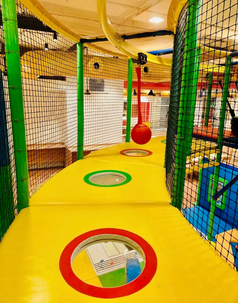 A colorful indoor playground with soft yellow pathways and netting, featuring holes for children to look through.