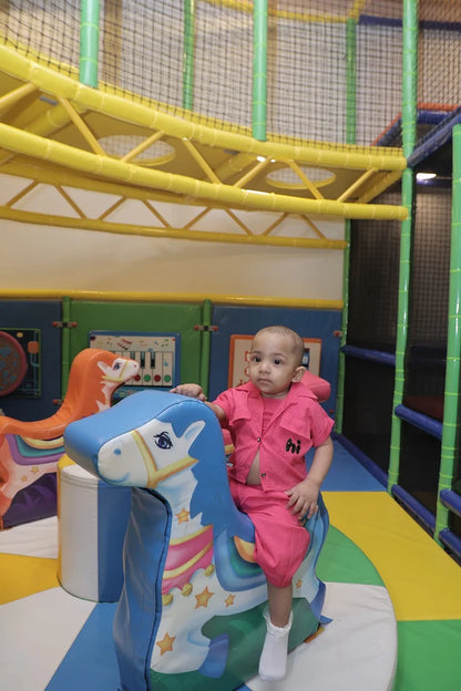 A young child sits on a blue toy horse in a colorful indoor playground.