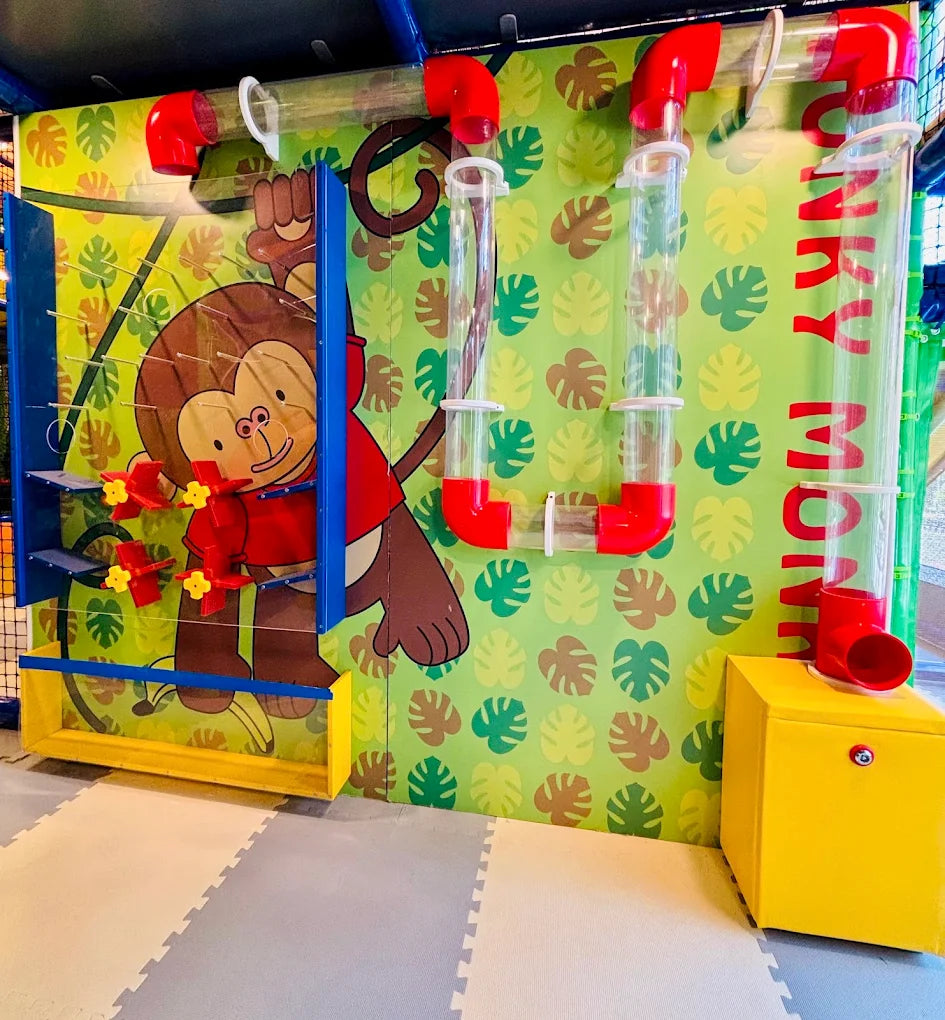 A colorful indoor playground with a monkey-themed wall, tubes, and a yellow storage box.