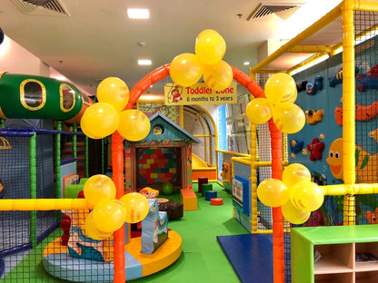 A colorful indoor playground with yellow balloons and a toddler zone.