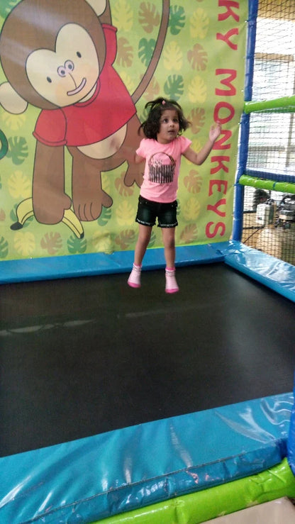 A young child jumps on a trampoline in front of a monkey-themed backdrop.