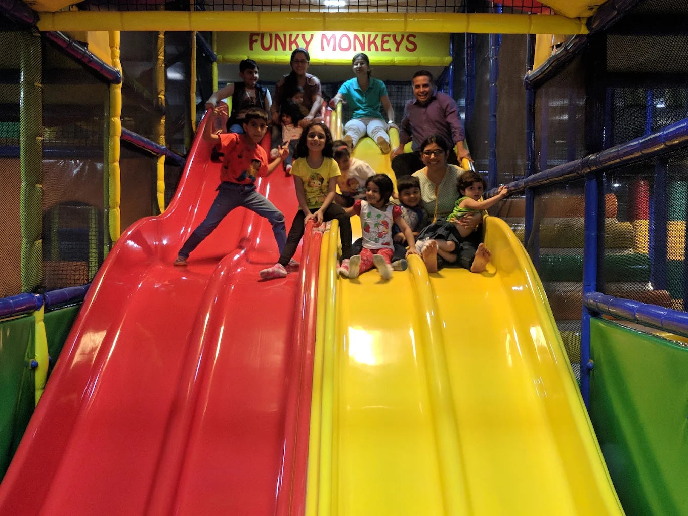 Children and adults slide down a red and yellow playground slide at Funky Monkeys.