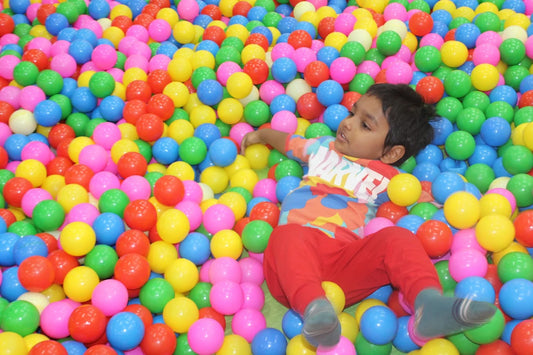 A young child lies in a ball pit, surrounded by colorful balls.