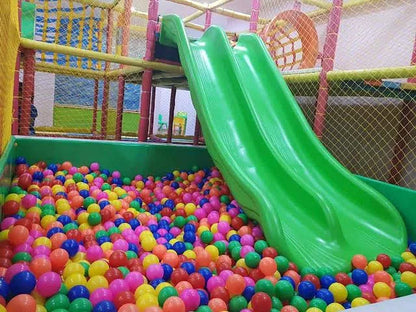 A bright green slide descends into a ball pit filled with colorful plastic balls, in a children's indoor play area.