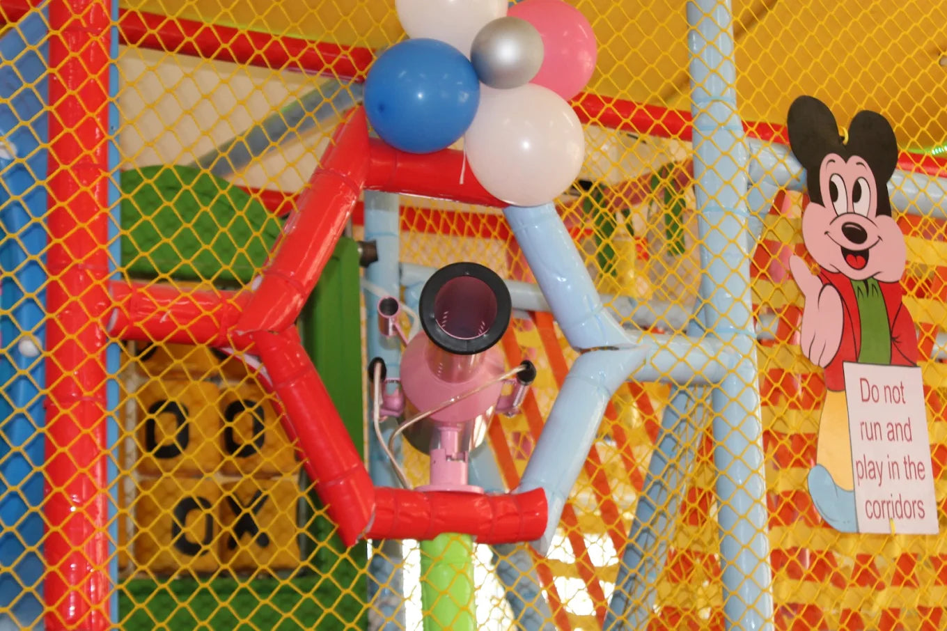 A colorful indoor playground with balloons, a Mickey Mouse cutout, and a sign warning children not to run.