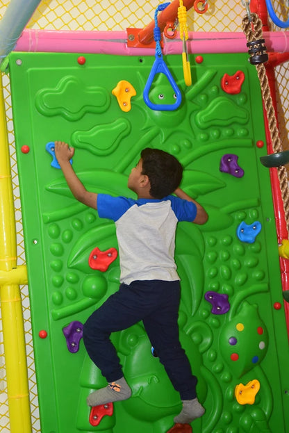 A young boy climbs a green rock wall with colorful handholds.