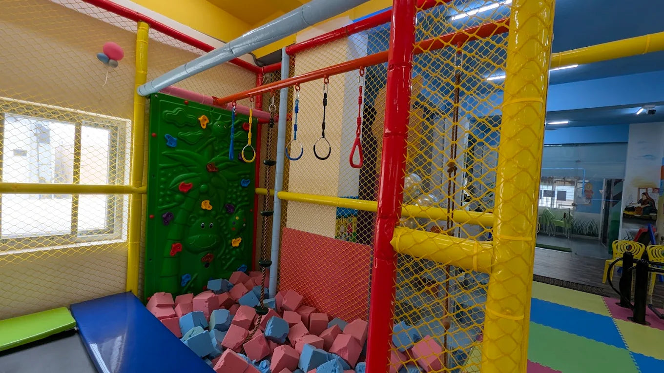 A colorful indoor playground with a ball pit, climbing wall, and hanging rings for children.