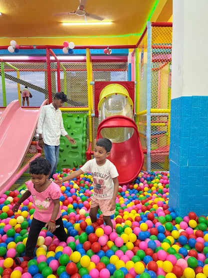 Children play in a colorful ball pit at an indoor playground.
