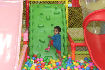 A young child climbs a green wall in a ball pit at a playground.
