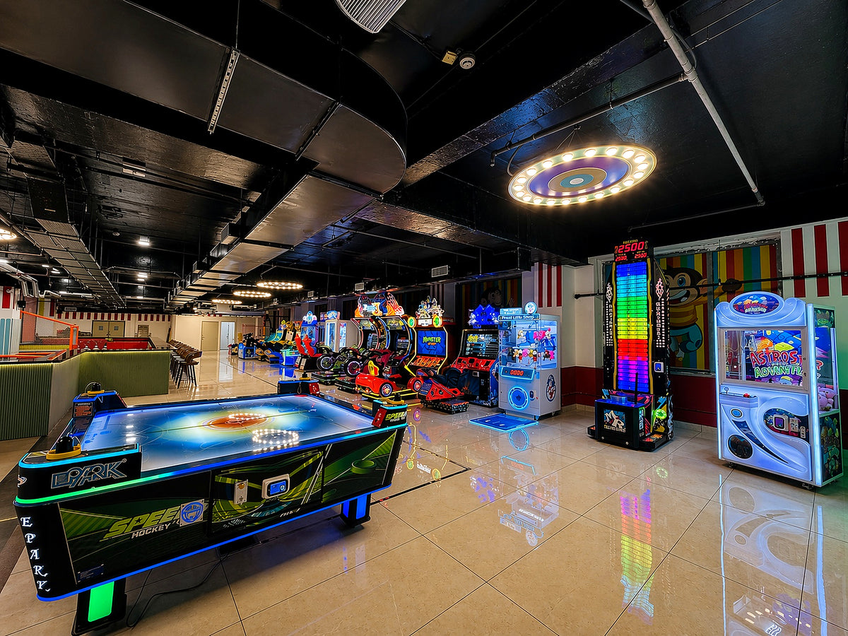 An arcade with various games, including an air hockey table and racing simulators, is brightly lit.