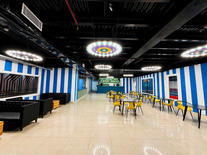 An empty indoor seating area with blue and white striped walls, black sofas, and yellow chairs around tables.