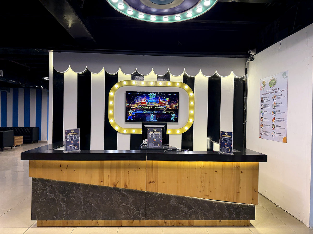 A brightly lit reception desk in an arcade with a large screen displaying games.