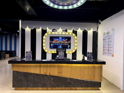 A brightly lit reception desk in an arcade with a large screen displaying games.