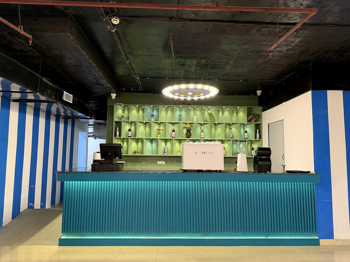 A modern bar with a teal counter and shelves stocked with bottles and decor.