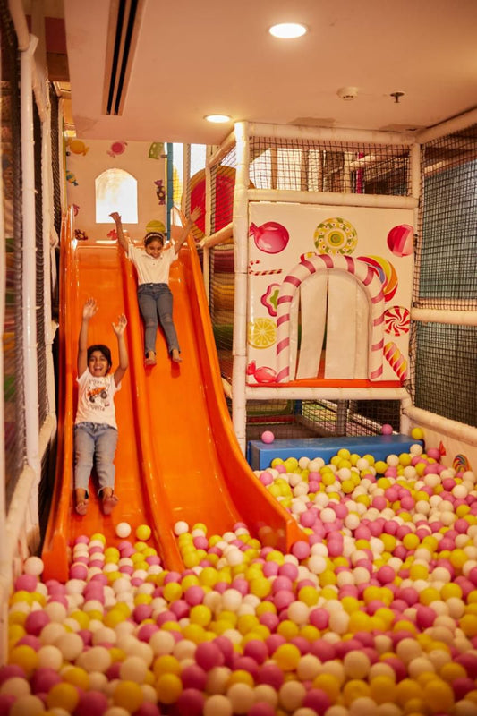 Children playing on an indoor slide with a ball pit filled with colorful balls.
