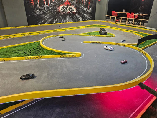 RC cars race on a track with yellow borders and green mossy areas, set against a city mural.