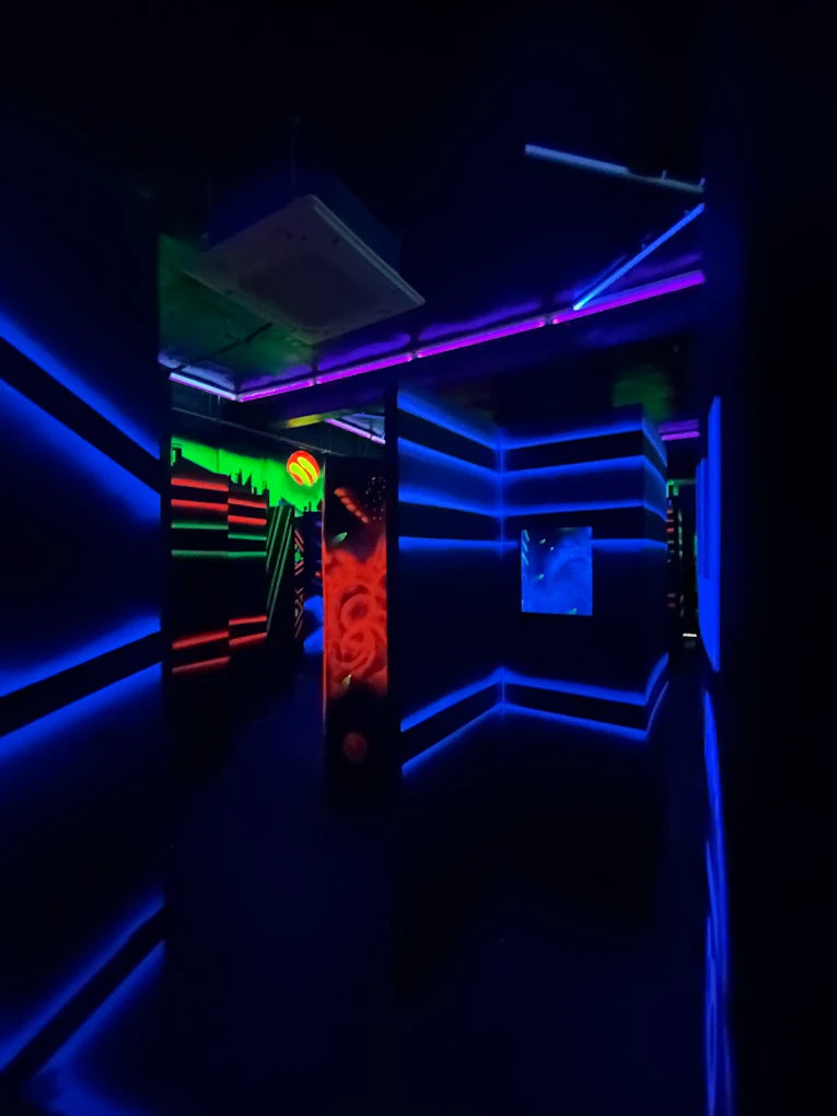 A dark laser tag arena with neon blue and purple lights, and glowing red and green accents.