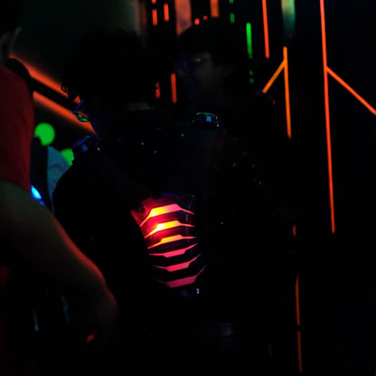 A person in a dark room with neon lights plays laser tag, wearing a vest with glowing red and yellow lights.