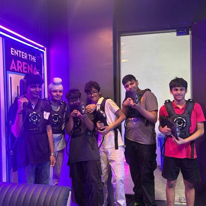 Young people in laser tag vests and gear pose for a photo in a dimly lit, neon-lit arena.