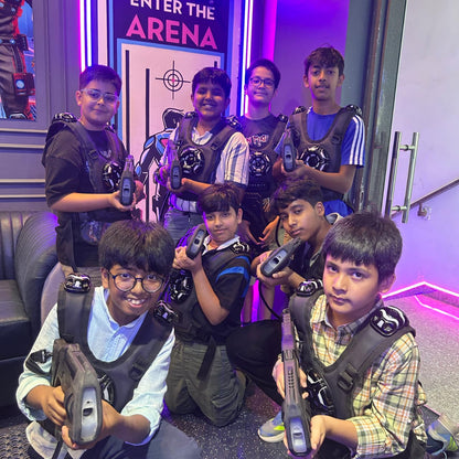A group of young boys in laser tag vests and holding phasers pose for a photo in a neon-lit arena.