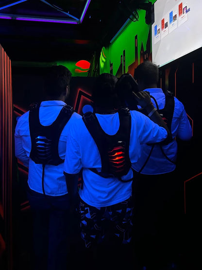 Three young adults in a dark laser tag arena wear illuminated vests, ready for a game.