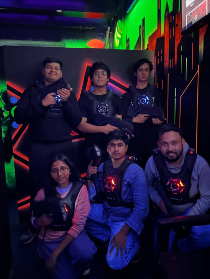 A group of young adults in laser tag vests and holding phasers pose for a photo in a neon-lit arena.