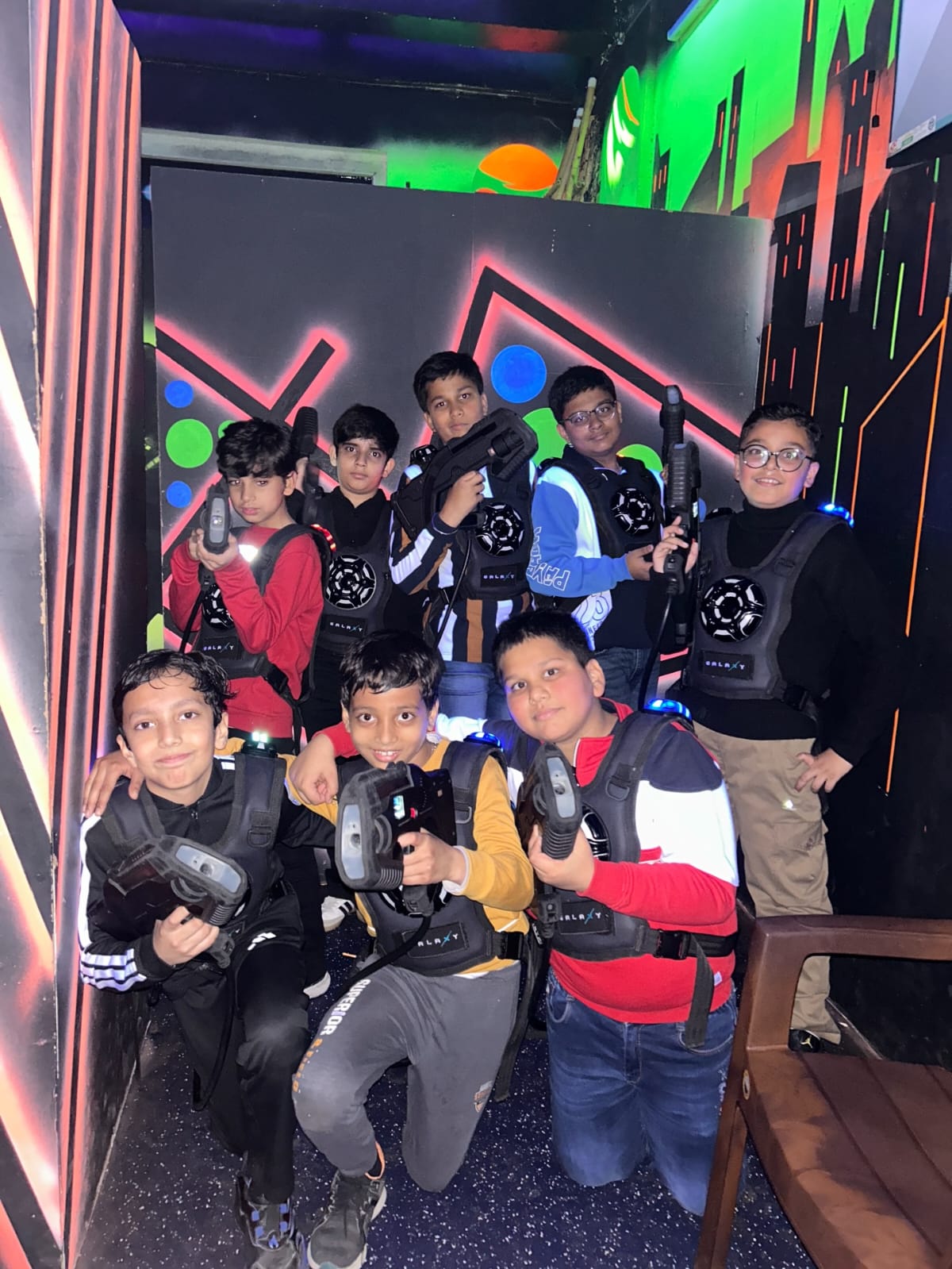 A group of young boys in laser tag vests and holding phasers pose for a photo in a neon-lit arena.
