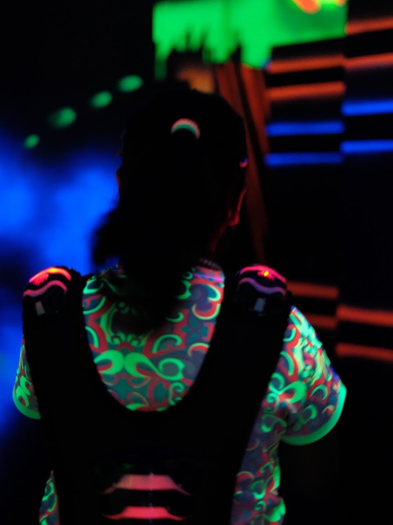 A person in a dark room wears a glowing vest with neon patterns, playing a game.