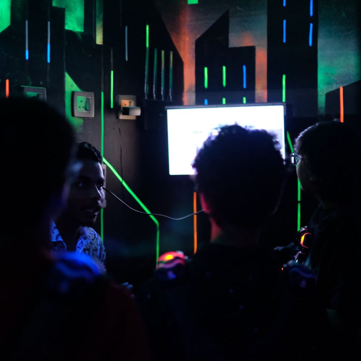 Young people play a video game in a dimly lit room with neon lights.