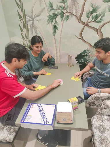 Three people playing a board game together in a room with decorative wall art.