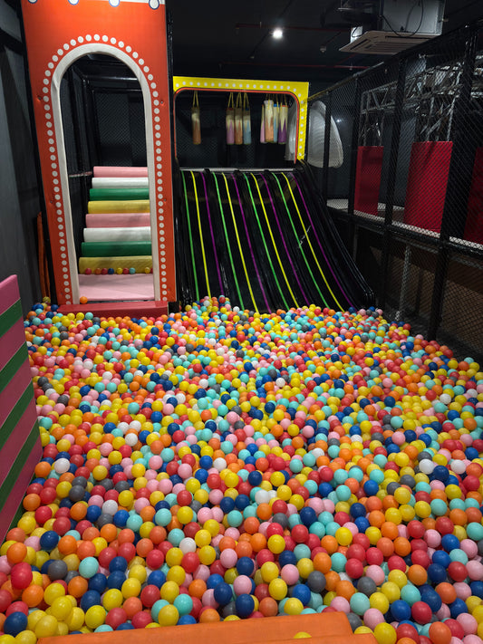 A ball pit filled with colorful balls, with a slide and climbing structure in the background.